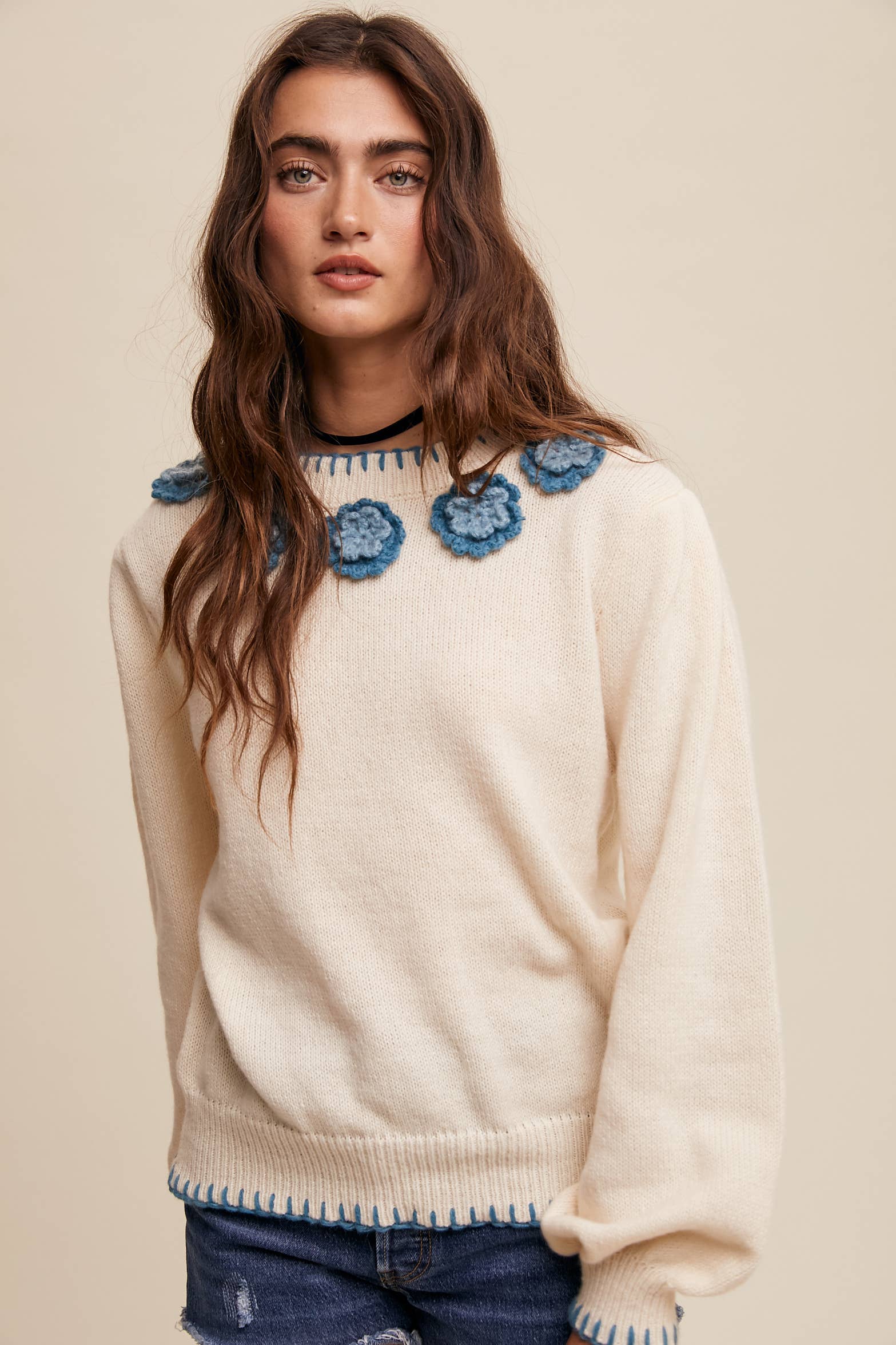 Cream sweater with blue crochet flower appliqués at neckline, blue whipstitch trim at cuffs and hem, long sleeves; styled with frayed denim shorts.