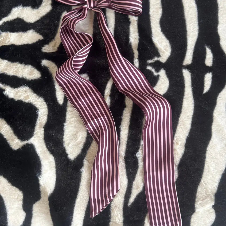 A burgundy and white striped ribbon tied into a bow, laid flat on a black and white zebra-print faux fur surface.