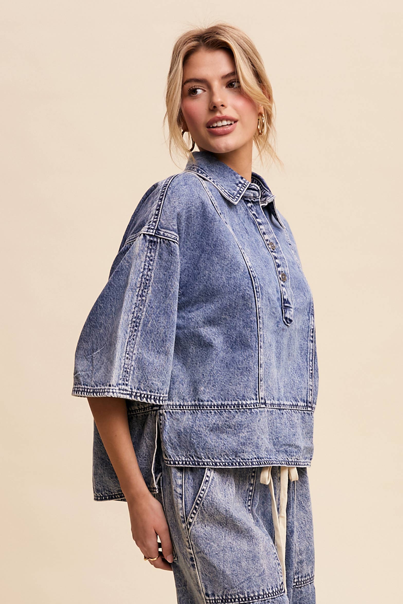 Side view- Light-wash denim pullover top with a half-button placket, exposed seam panels, and wide elbow-length sleeves in a relaxed, boxy fit.