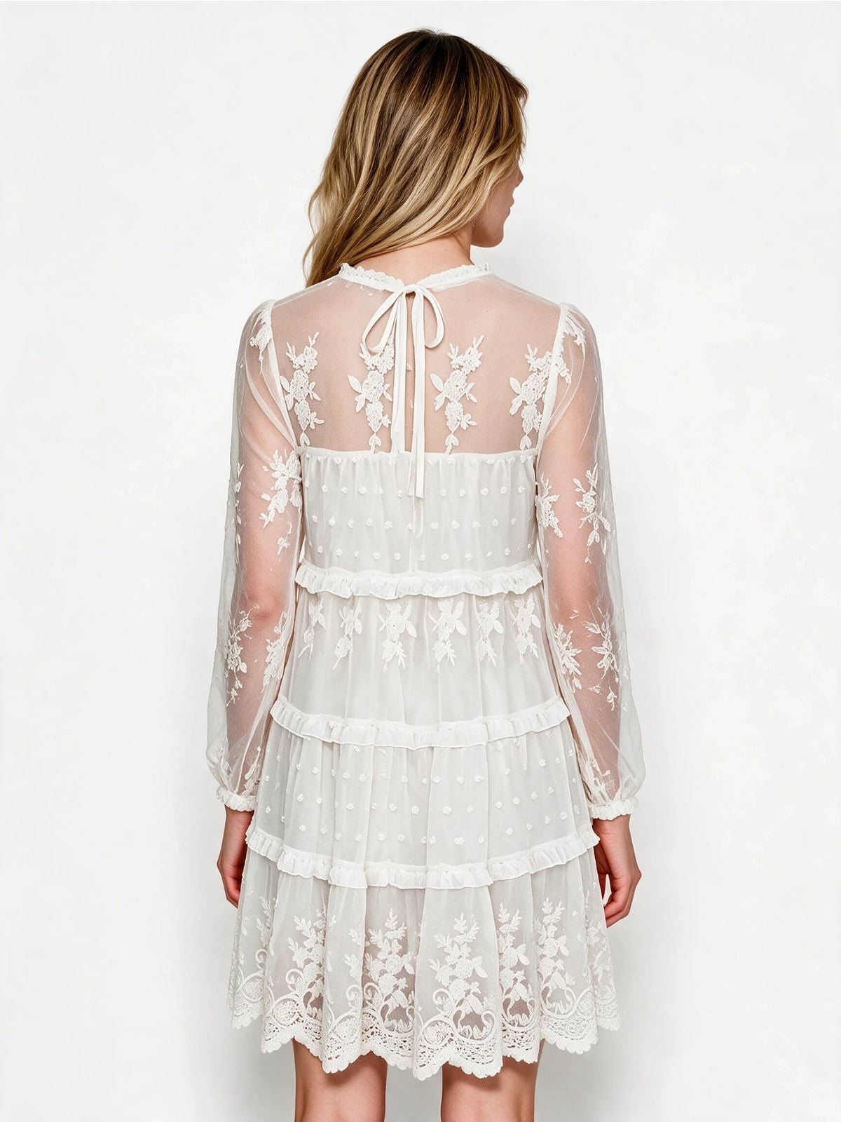 Back view of the white lace dress showing a keyhole tie closure, sheer embroidered upper back, and ruffle-trimmed tiers.