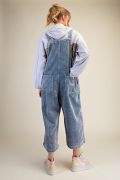 Back view of woman wearing light blue washed corduroy wide-leg overalls with floral patchwork, showing relaxed oversized silhouette and back pockets