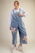 Full-length front view of woman in light blue floral patch corduroy wide-leg overalls with adjustable straps, layered over a white hoodie