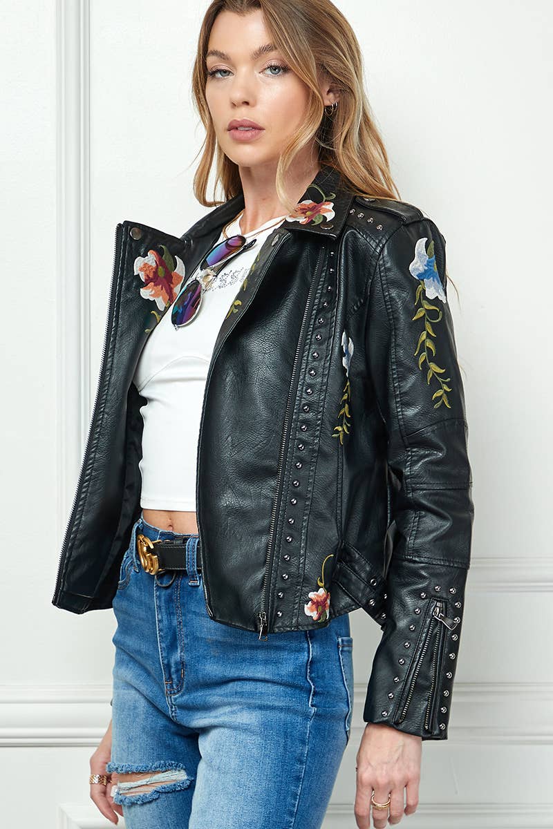 Black faux-leather moto jacket with floral embroidery and silver studs, styled with a white crop top and high-waisted blue jeans.