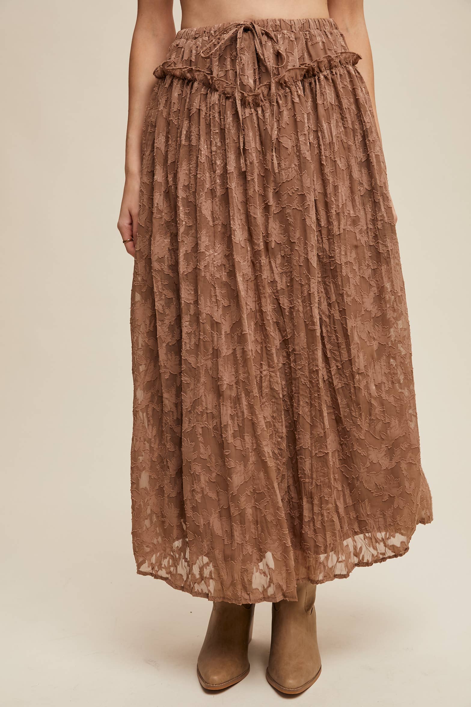 Mocha brown floral lace maxi skirt with drawstring waist, ruffle trim, and subtle bubble hem, styled with tan heeled ankle boots.