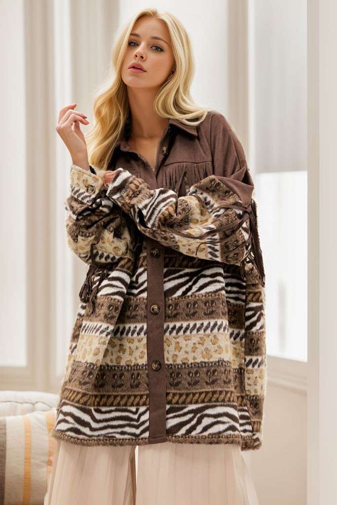 Brown Aztec print shacket with fringe detailing, button-front closure, and long sleeves, styled over a white strapless top and cream pleated pants.