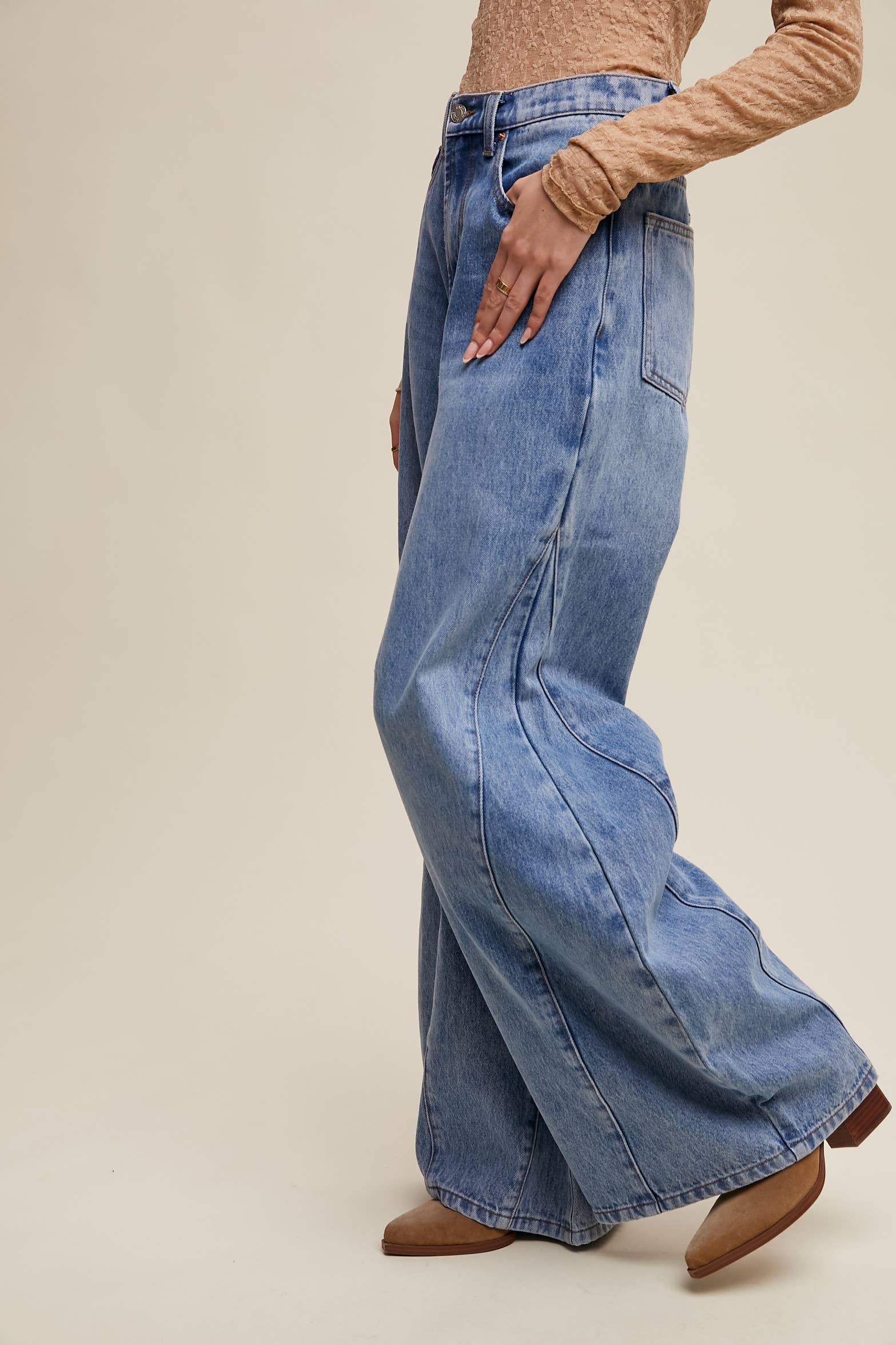 Side view- High-rise light-wash wide-leg jeans with front seam panels and knee darts, five-pocket style with zip fly, styled with tan long-sleeve top and pointed-toe boots.