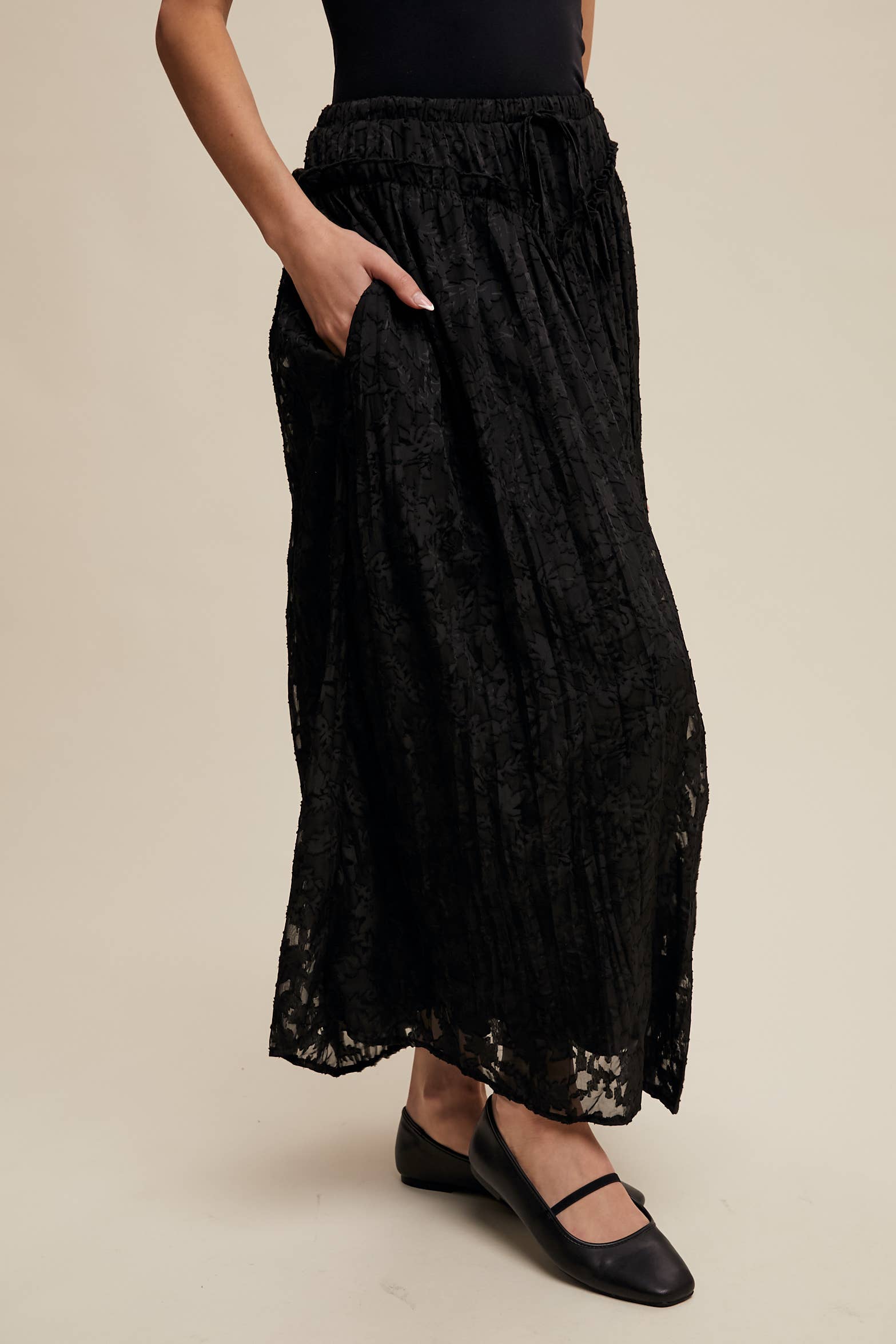 Black floral lace maxi skirt with elastic drawstring waist, ruffle trim and pockets; semi-sheer bubble hem, styled with black Mary Jane flats.