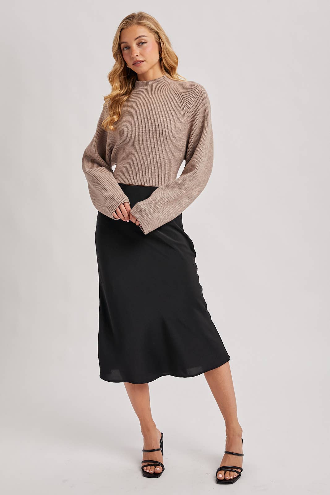 Taupe ribbed mock-neck sweater with wide long sleeves and a cropped fit, styled with a black skirt.