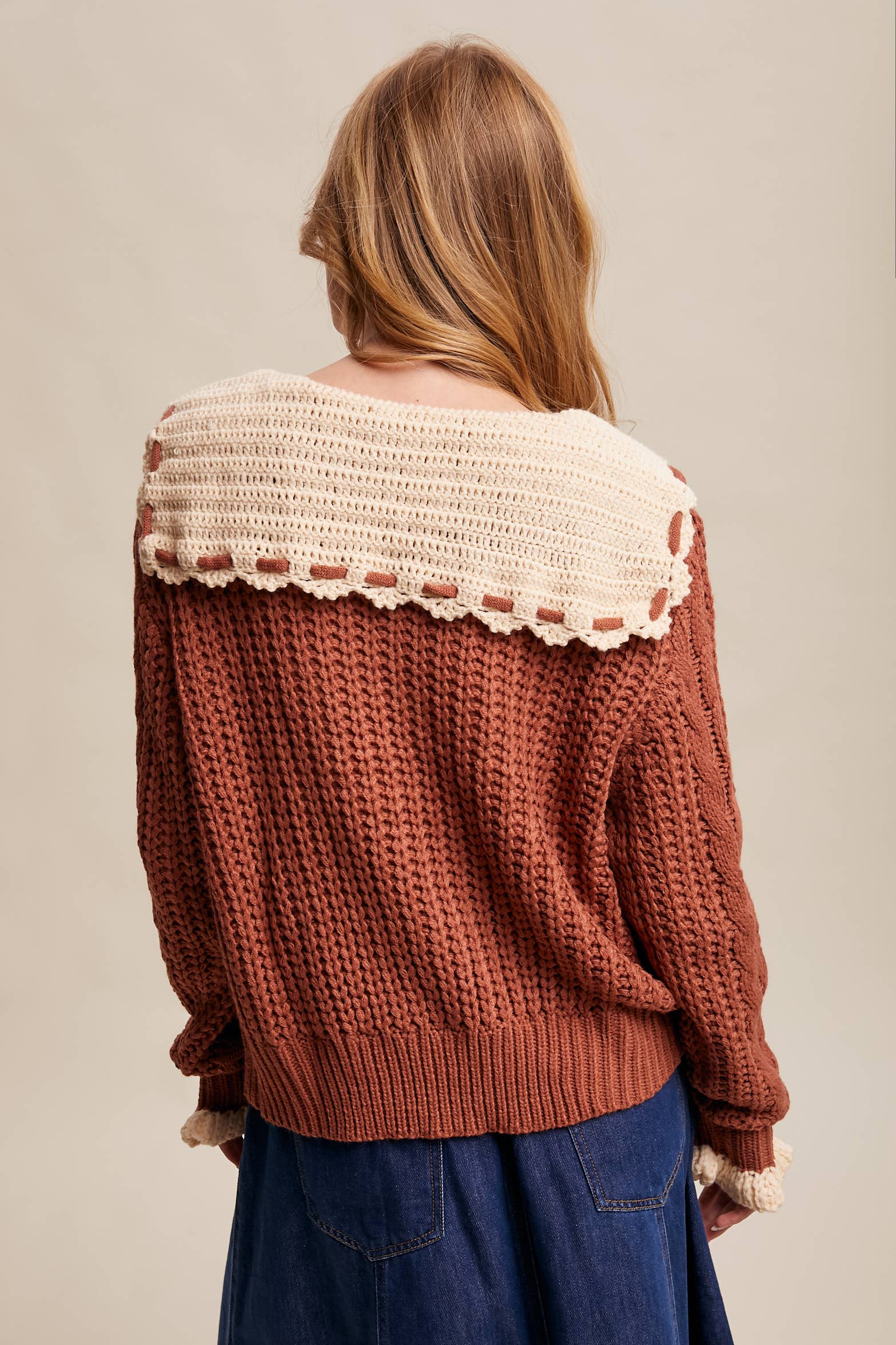 Brown knitted sweater with lace trim worn by a person on a beige background