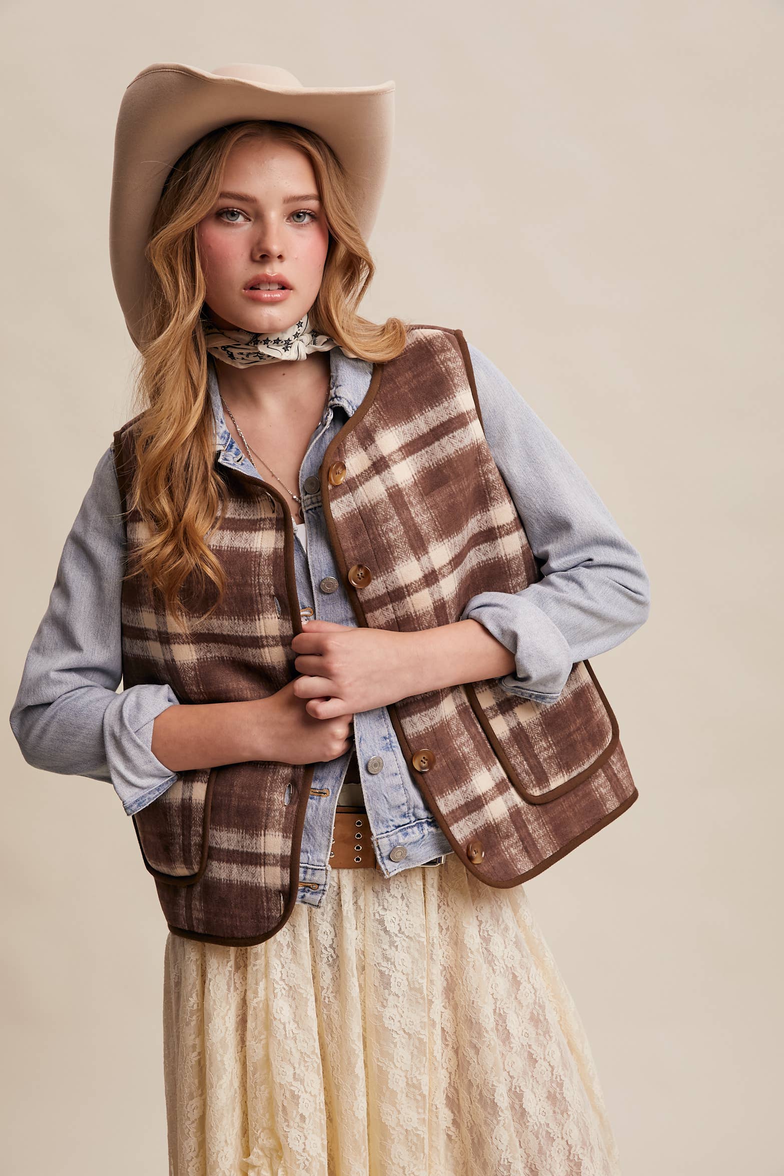 Woman wearing a plaid vest, hat, and skirt on a beige background
