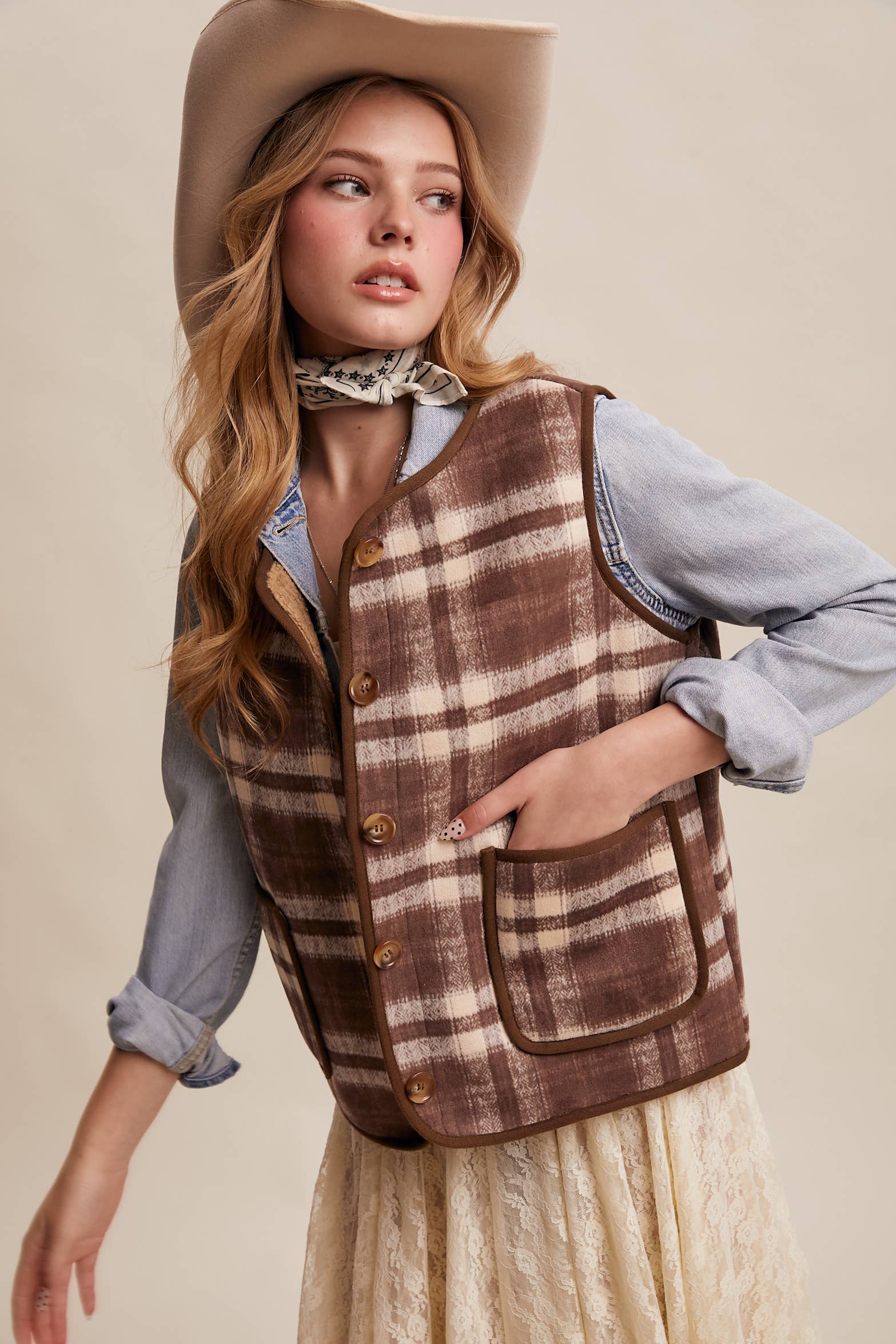 Woman wearing a plaid vest and hat on a beige background