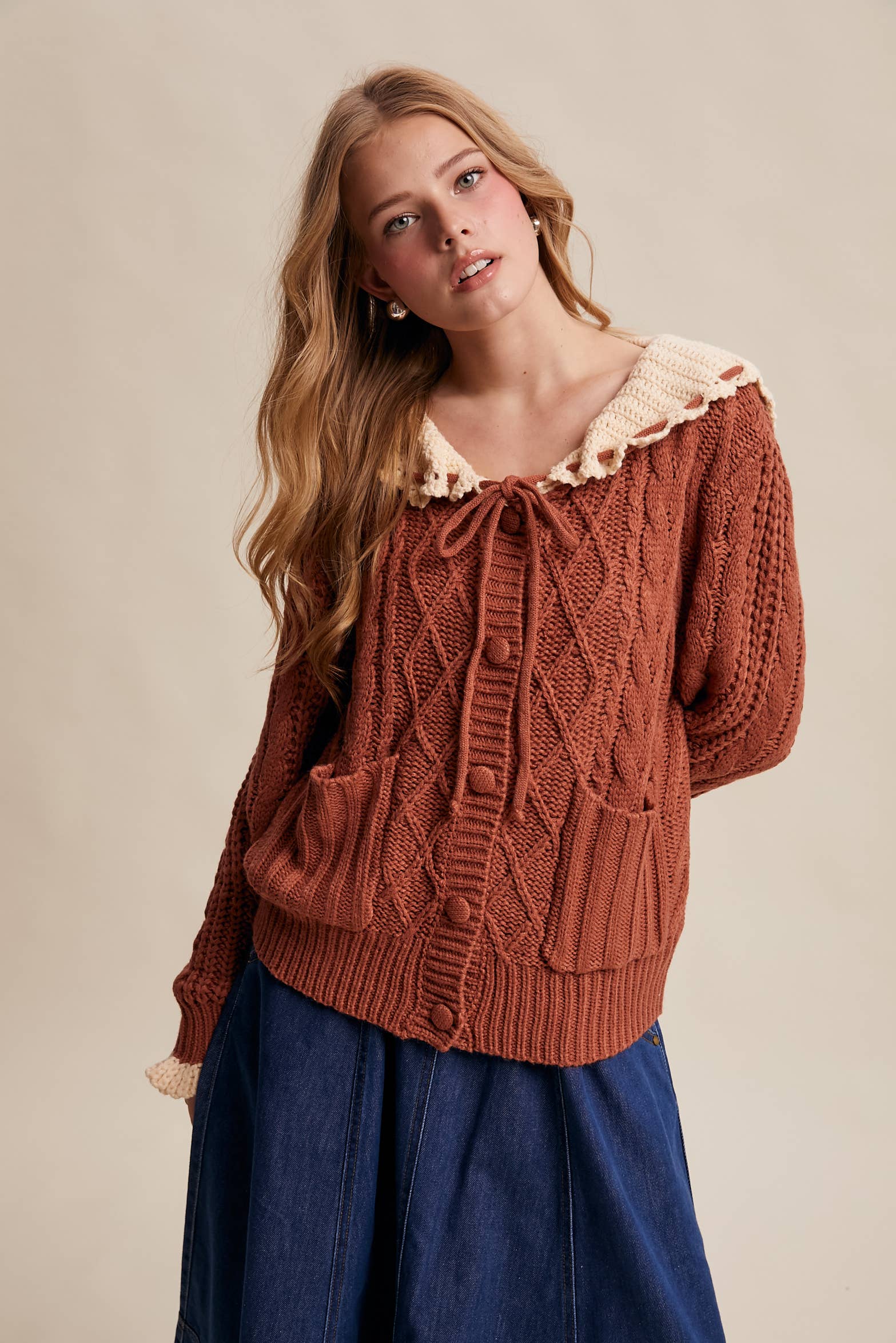 Woman wearing a brown knitted sweater with lace trim on a beige background