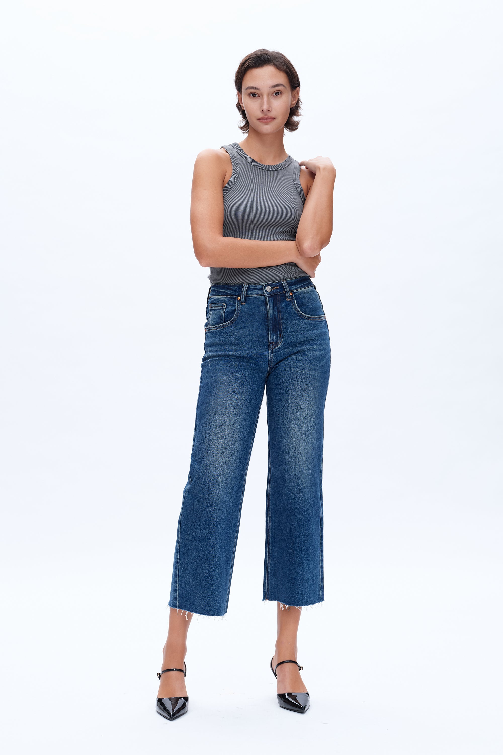 Woman wearing a gray tank top and blue jeans on a white background