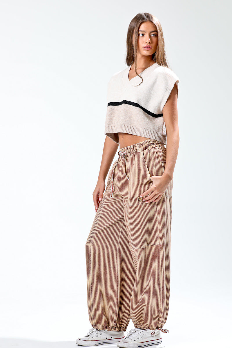 Woman wearing a white and black top with beige striped pants on a white background