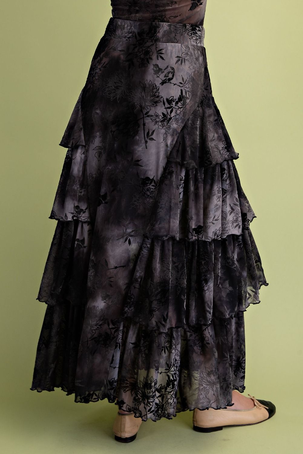 A black and gray tie-dye tiered maxi skirt with a floral pattern, shown on a model against a solid olive green background.