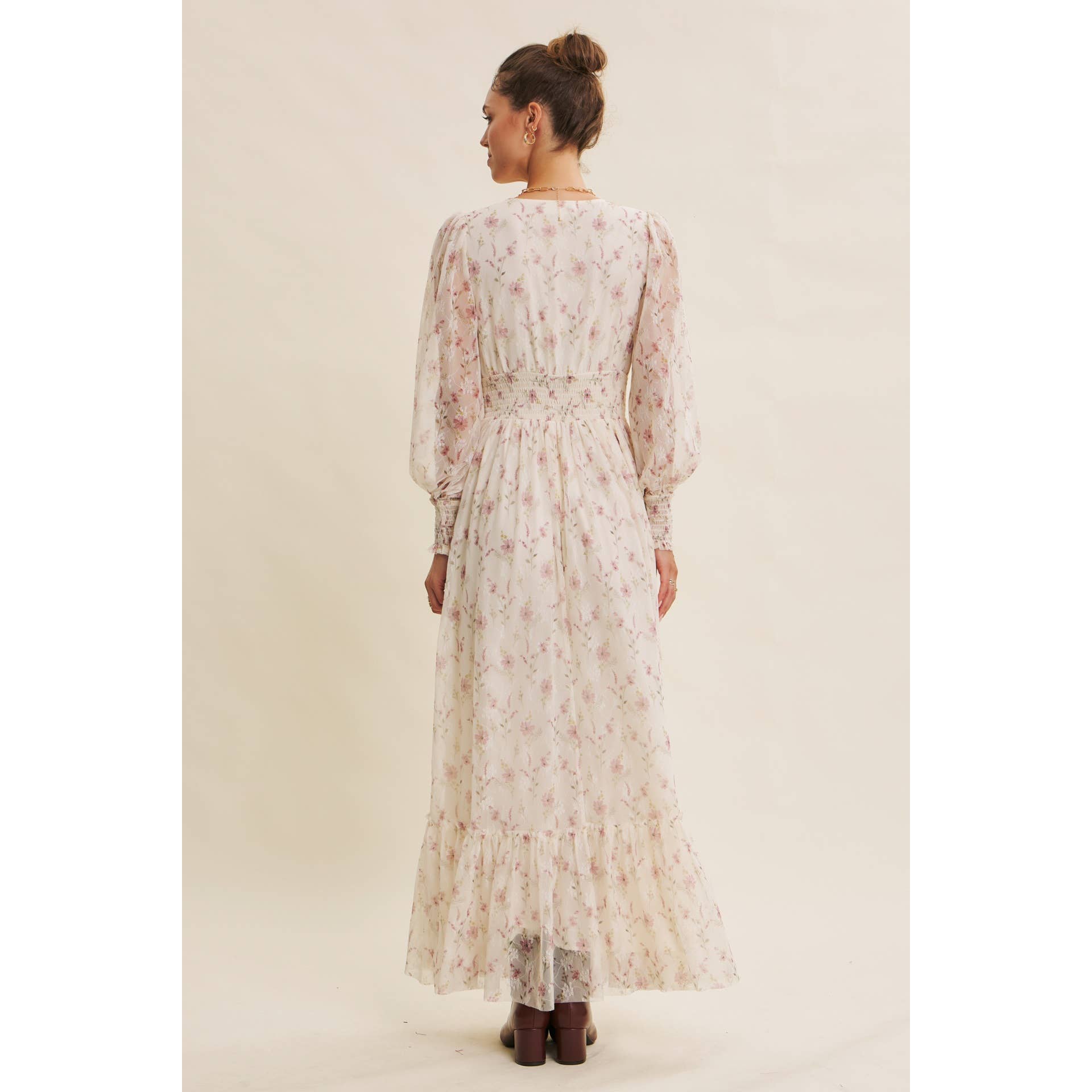 Back view — cream floral chiffon maxi dress with V-neck, sheer long sleeves, smocked waist, and ruffle hem; styled with brown boots.