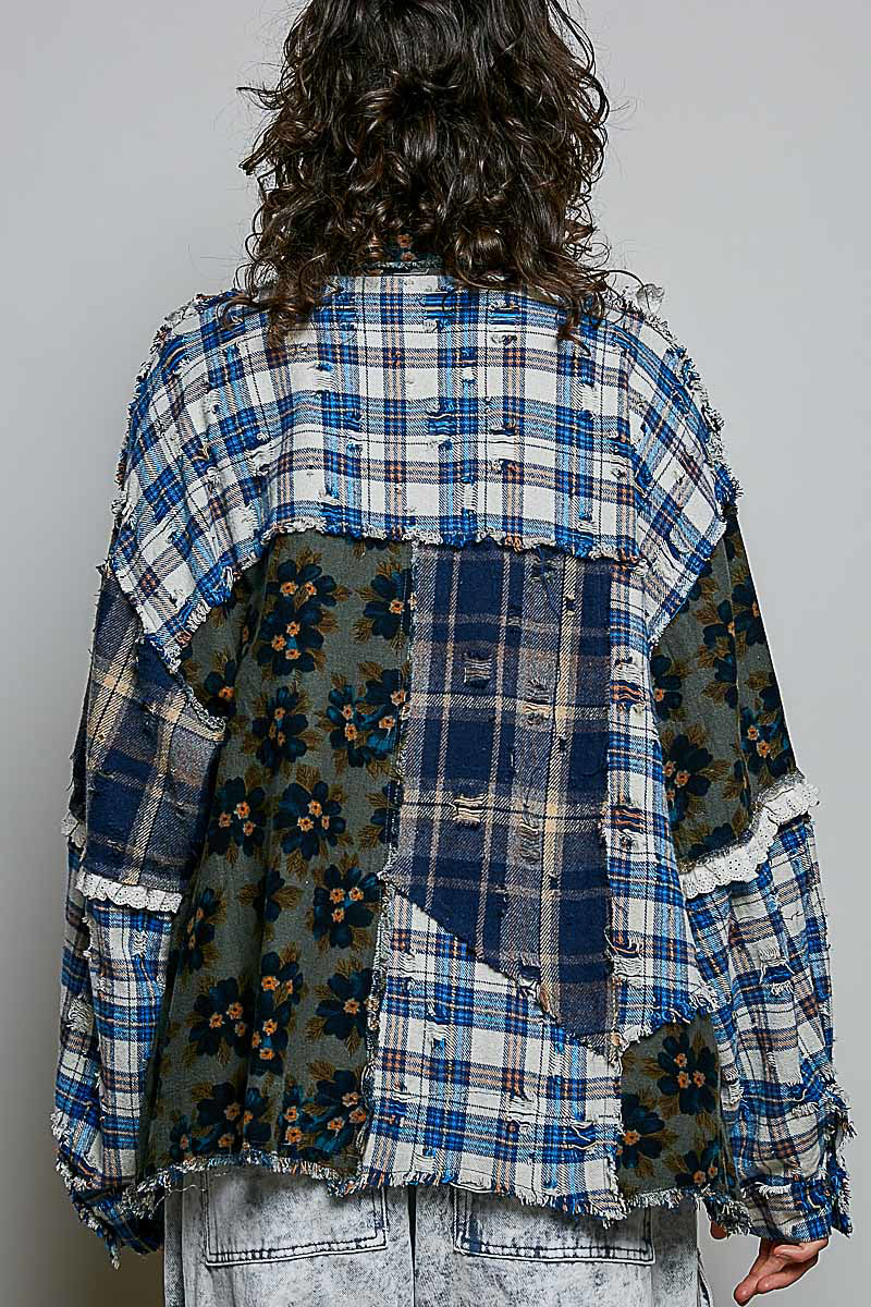 A person shown from the back wearing a patchwork patchwork shirt with blue plaid, floral green, and navy sections, paired with light-wash jeans against a plain gray background.