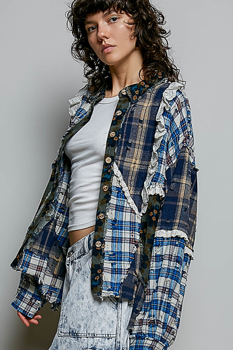 A model wearing a blue and beige plaid button-up shirt jacket with ruffle details, layered over a white crop top and light-wash denim jeans, set against a plain gray studio background.
