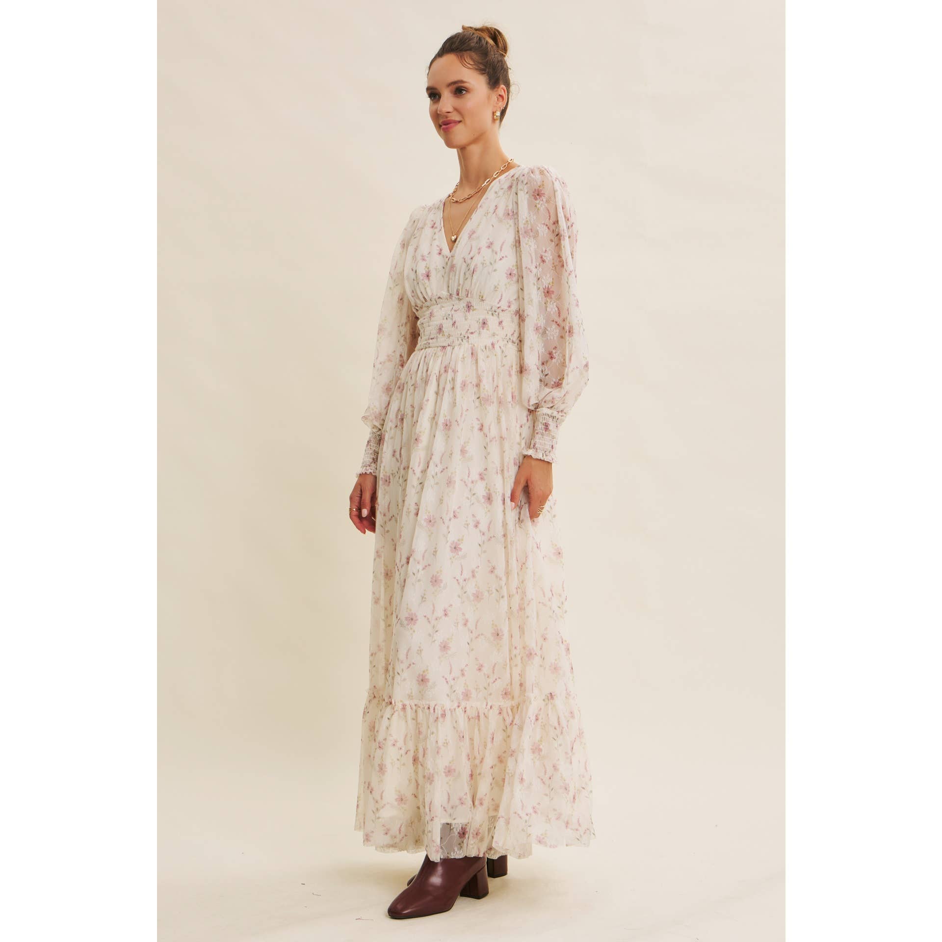 Side view — cream floral chiffon maxi dress with V-neck, sheer long sleeves, smocked waist, and ruffle hem; styled with brown boots.