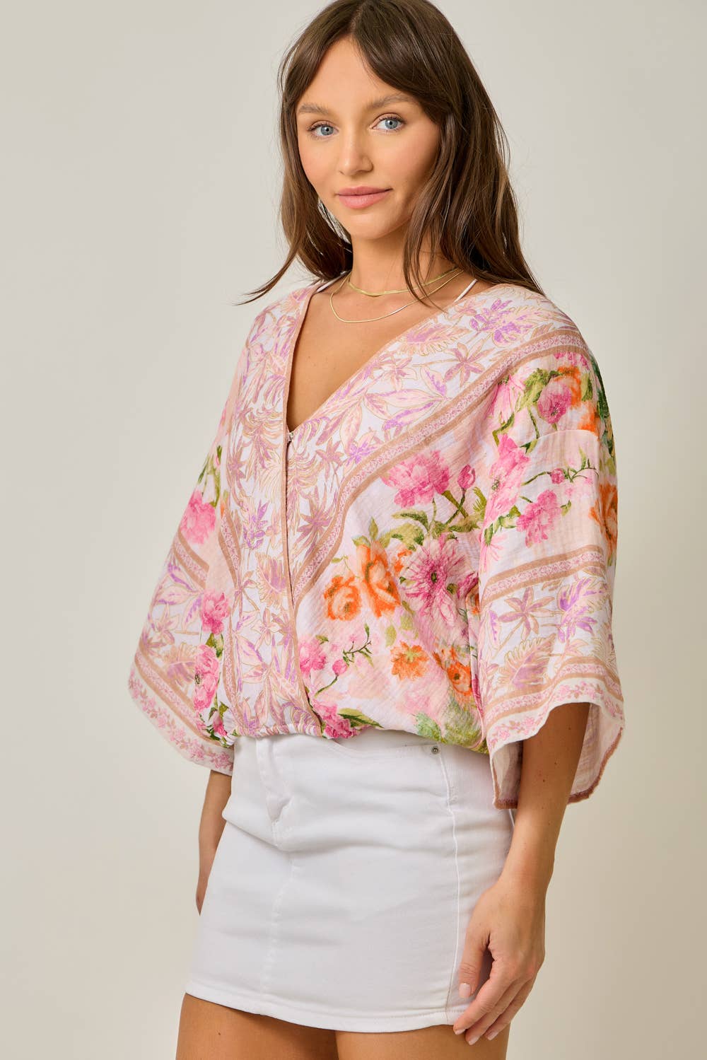 Woman wearing a floral blouse and white skirt against a plain background