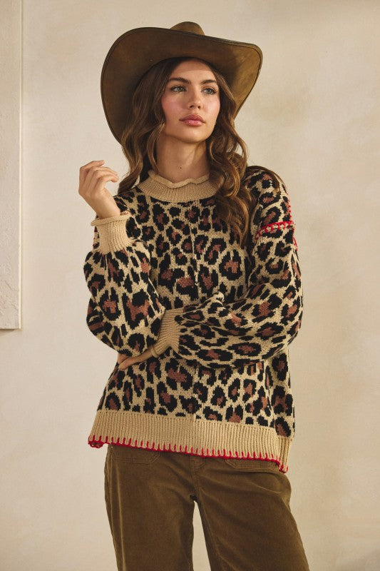 Leopard print knit sweater in tan with ribbed crew neck, cuffs and hem and red whipstitch trim, styled with brown corduroy pants and a cowboy hat.