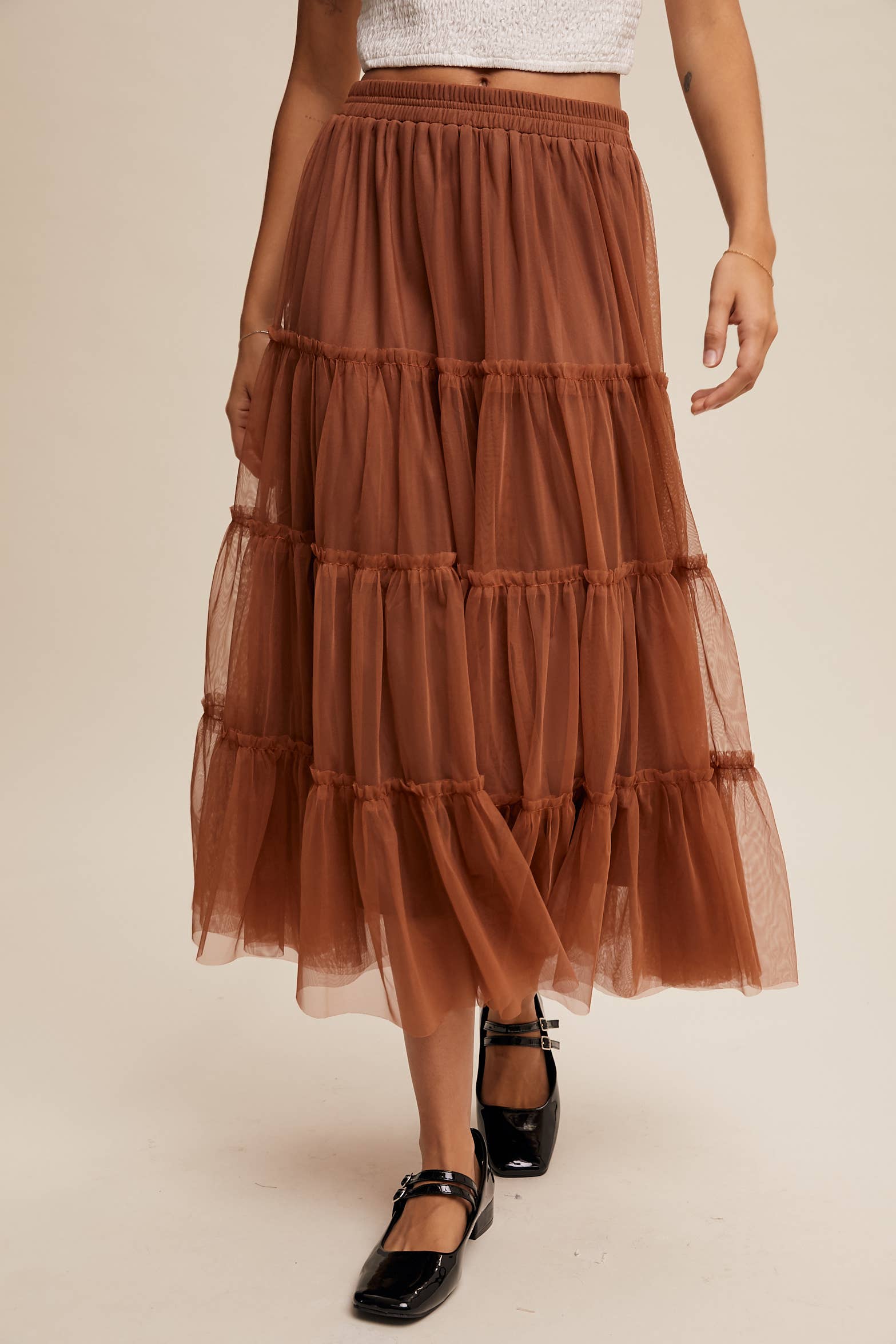 Close-up — rust tulle tiered midi skirt with elastic waist and ruffled layers, sheer overlay, styled with black Mary Jane flats.