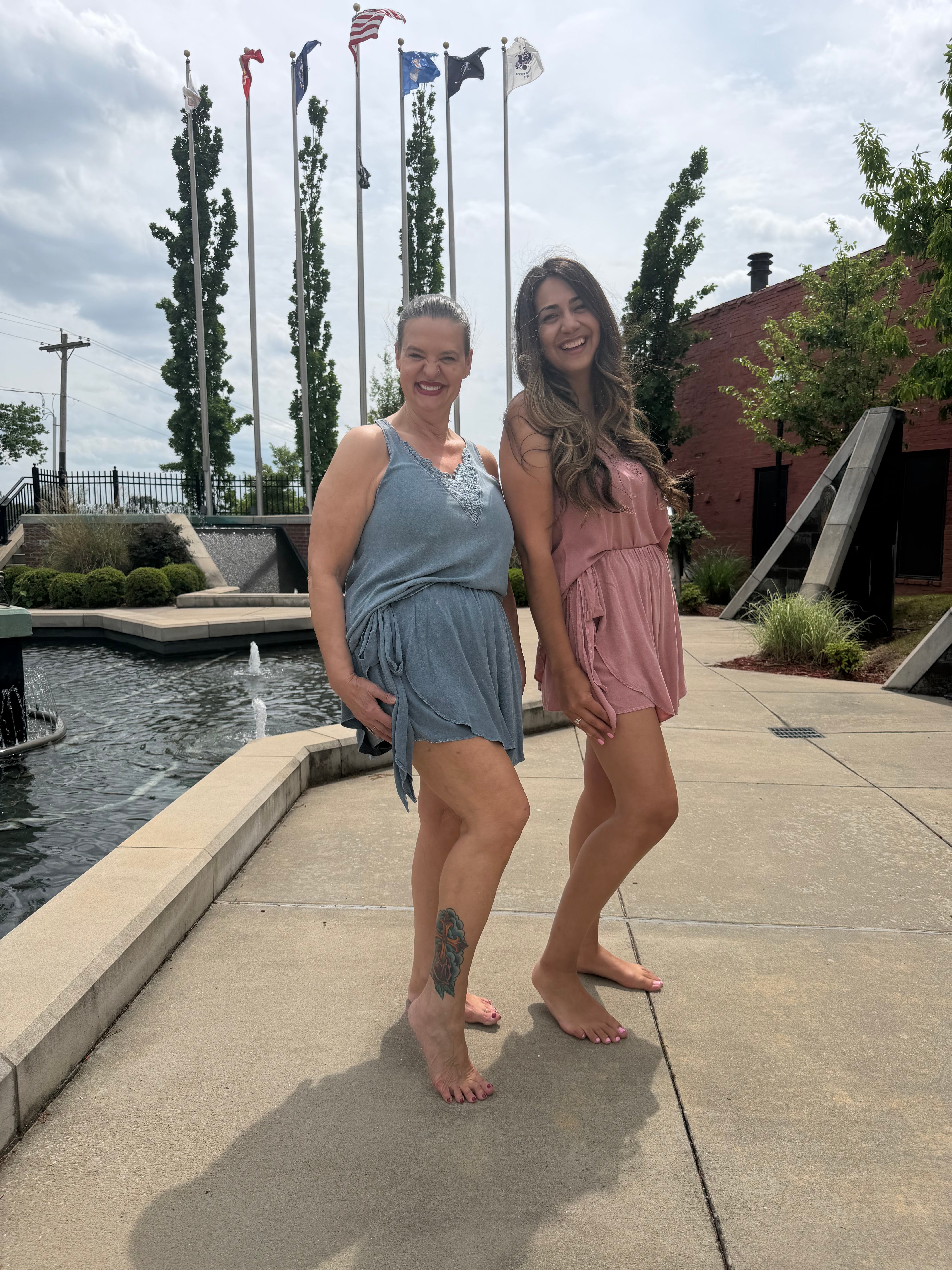 Two people standing on a sidewalk with a fountain and flags in the background.