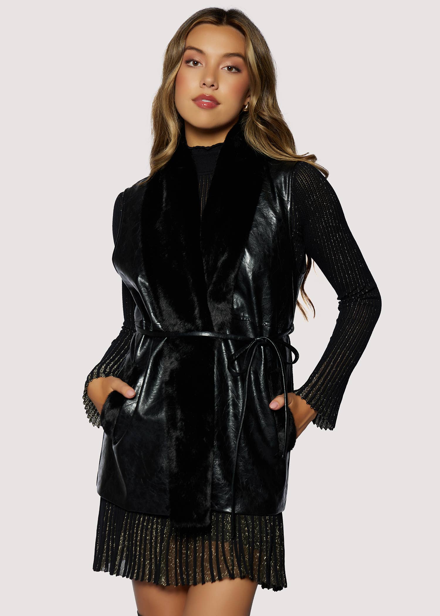 Woman wearing a black leather dress with fringe details on a light pink background