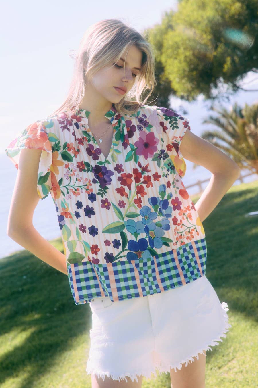 Woman wearing a colorful floral blouse and white shorts outdoors.