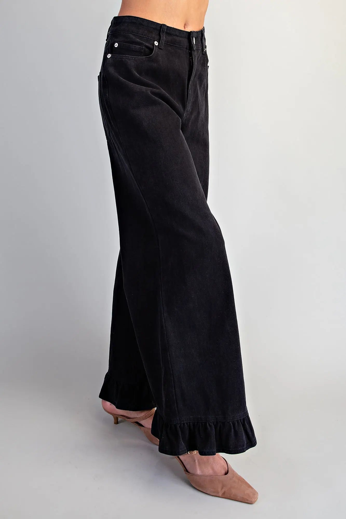 Side view of women's black wide-leg denim pants showing dramatic flare silhouette and ruffled hem detail, paired with nude kitten heel mules 