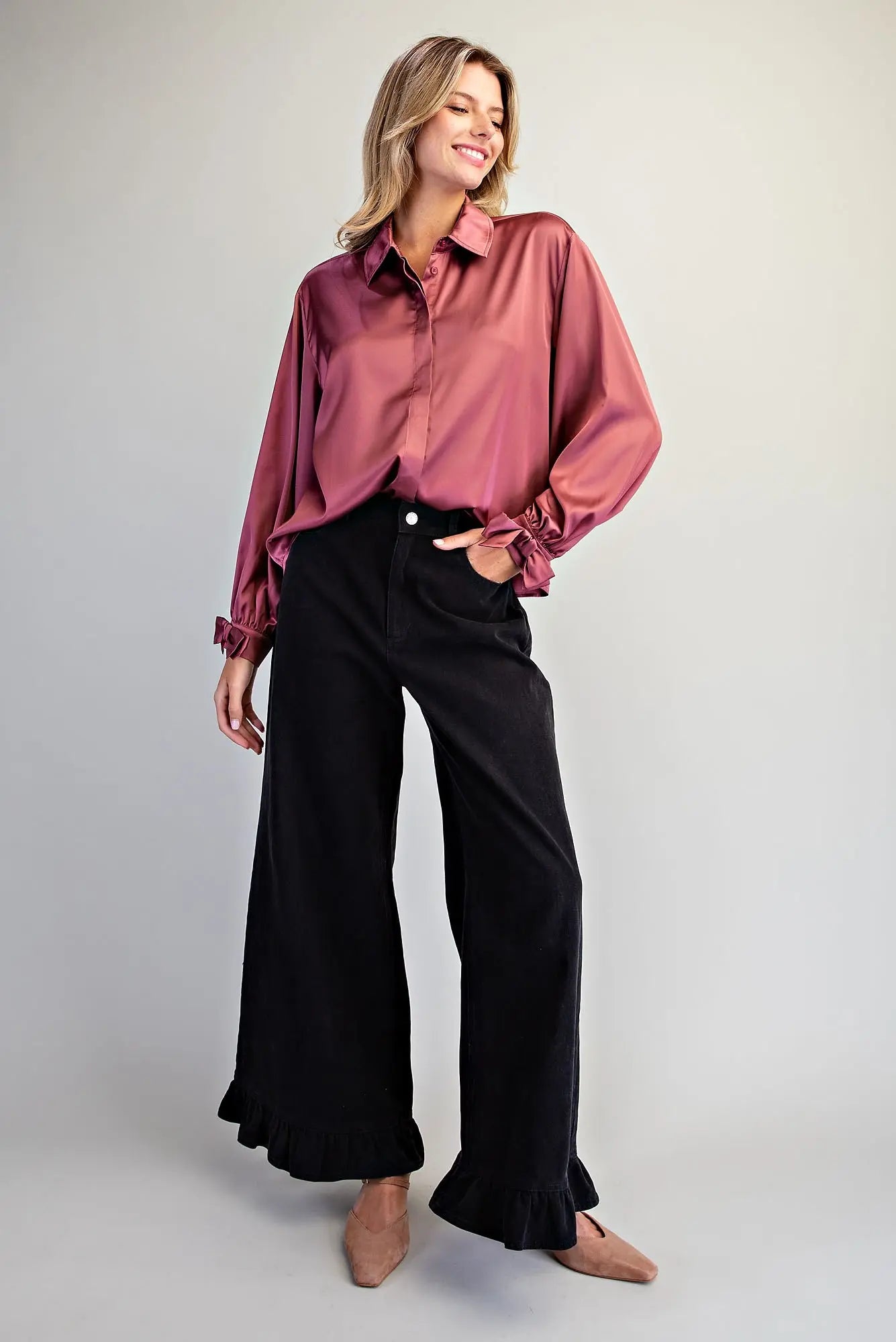 Full-length view of black wide-leg ruffle hem denim pants styled with a mauve satin button-down shirt and nude flats 