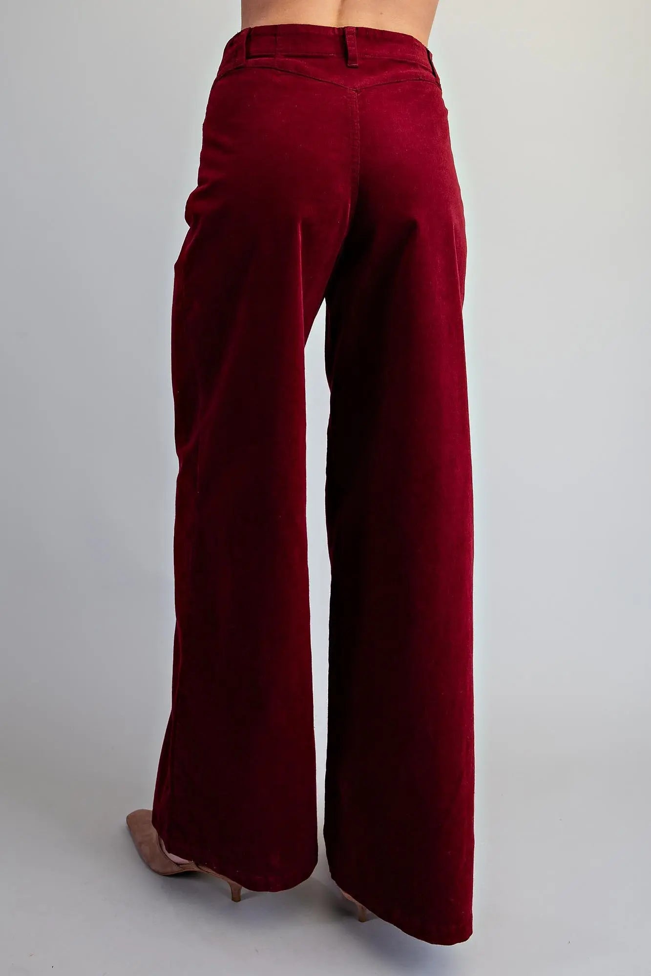 Back view of women's crimson high-rise wide-leg corduroy pants with belt loop waistband and clean seam detail, styled with nude heels 