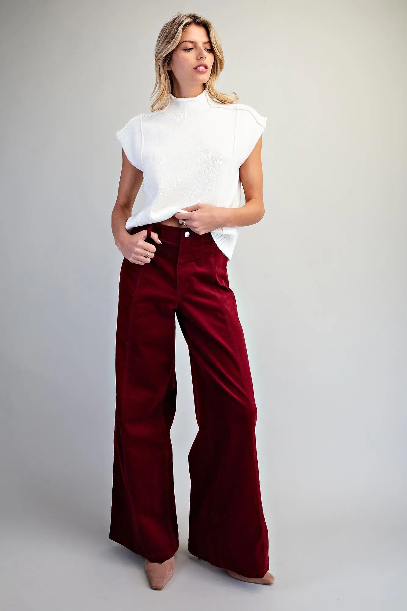 Full-length front view of crimson wide-leg corduroy pants styled with a white mock-neck sleeveless top and nude heels