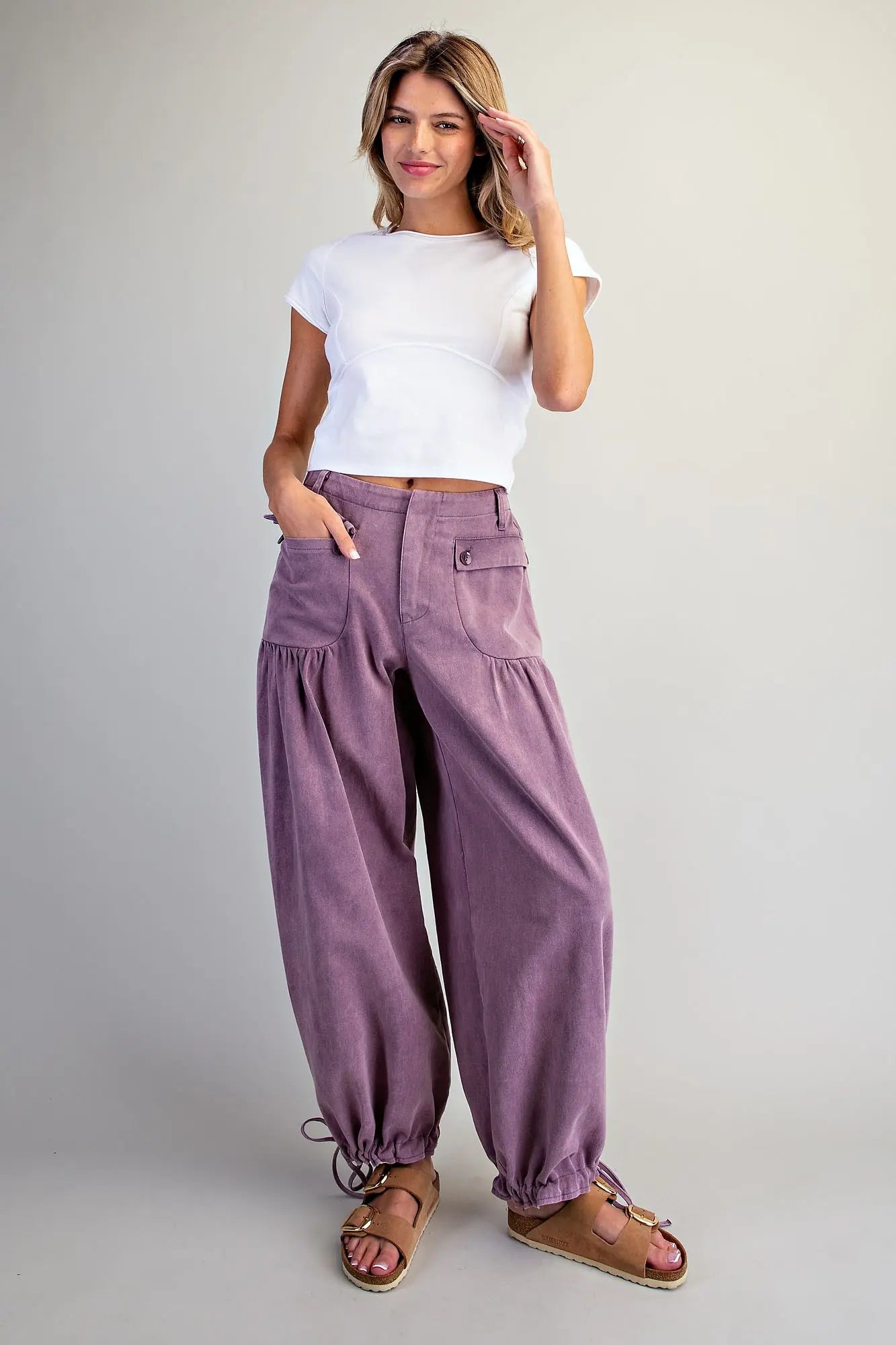 Full-length front view of women's plum mineral washed tie cuff pants — relaxed boho barrel leg with ruched pocket detail, styled with white crop tee and sandals