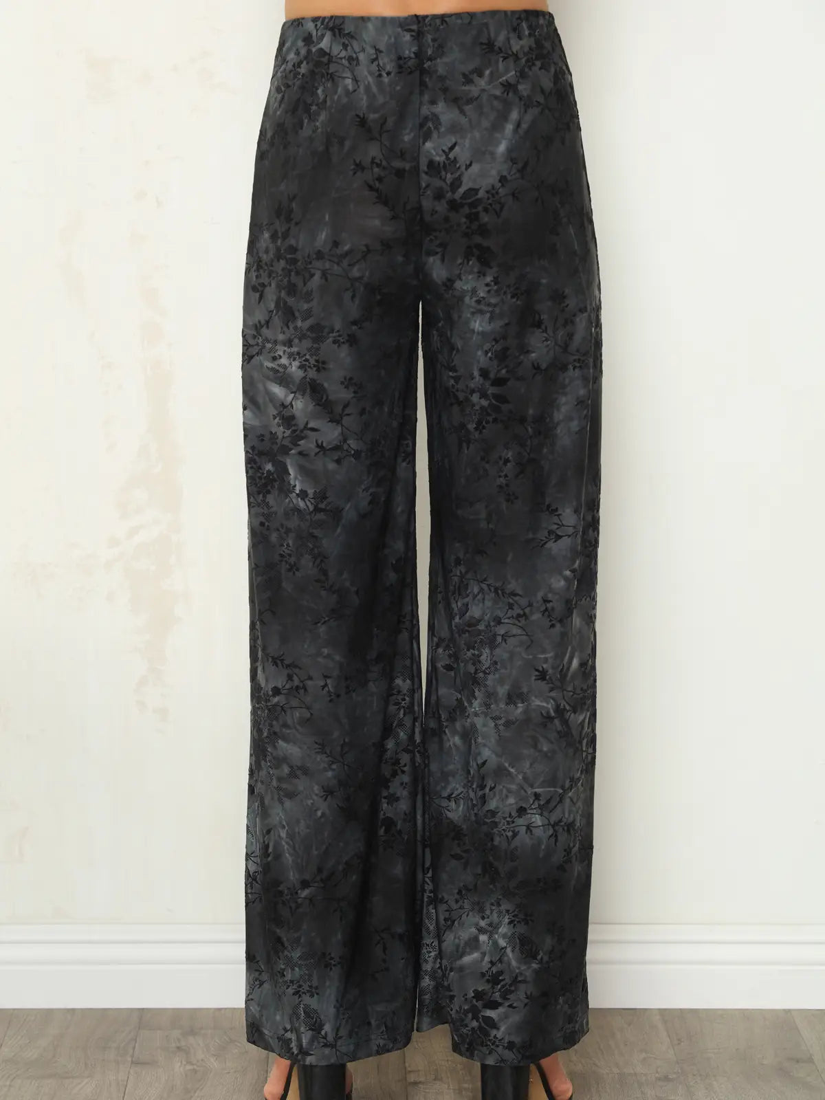 Black and gray floral jacquard wide-leg pants shown on a model from the waist down, standing against a light beige wall.