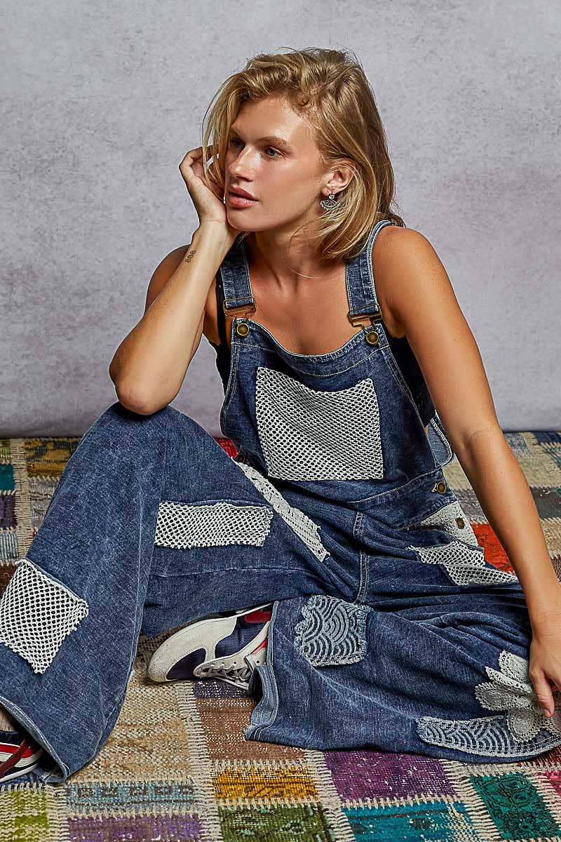 Boho denim patchwork overalls featuring wide legs, crochet lace appliqué patches, and vintage-inspired distressed detailing. Styled with a black crop top and sneakers for a relaxed, eclectic look.