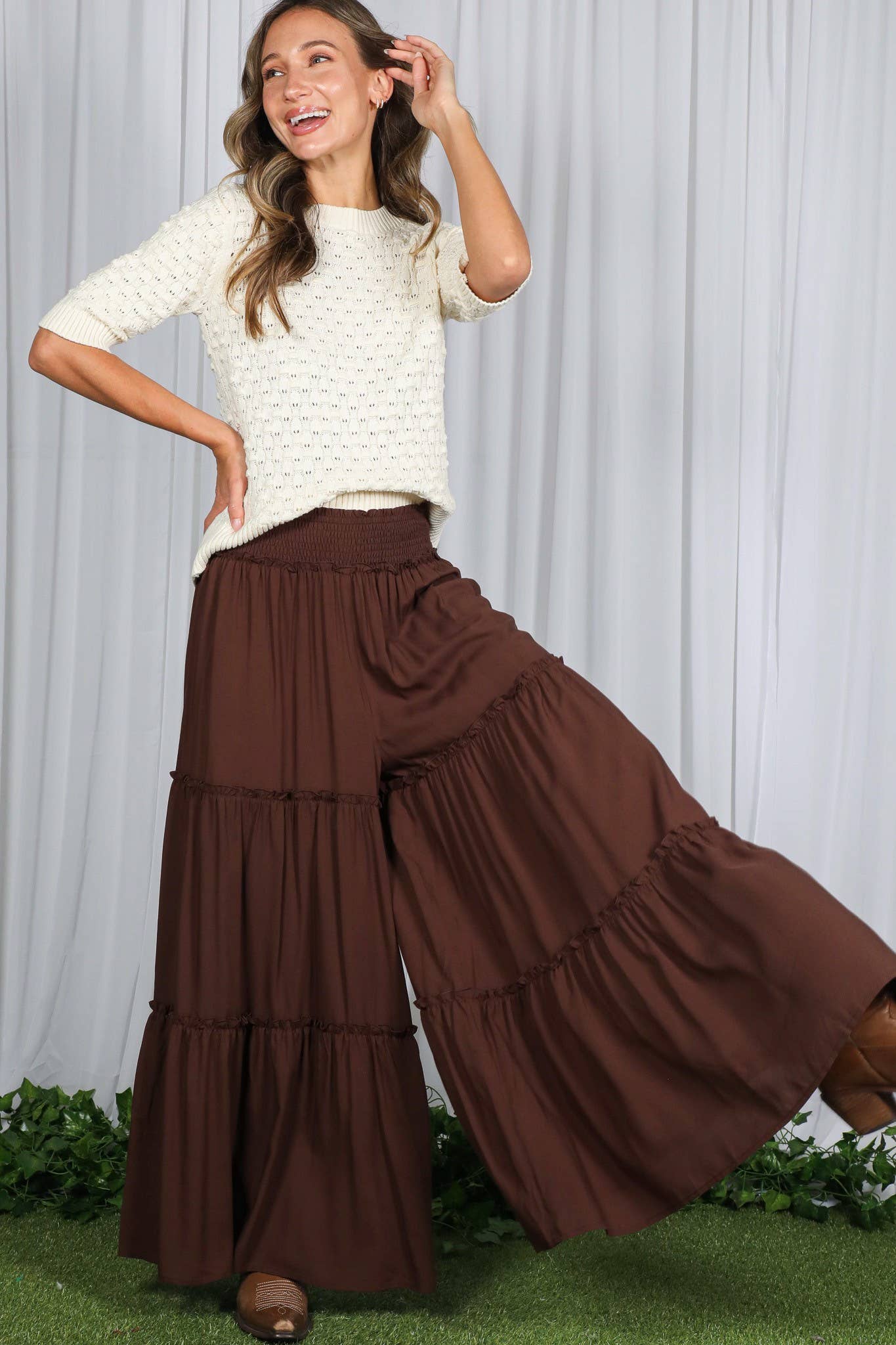 Woman wearing tiered palazzo pants with smocked waistband in mocha and black, styled for fall with sweater and boots.