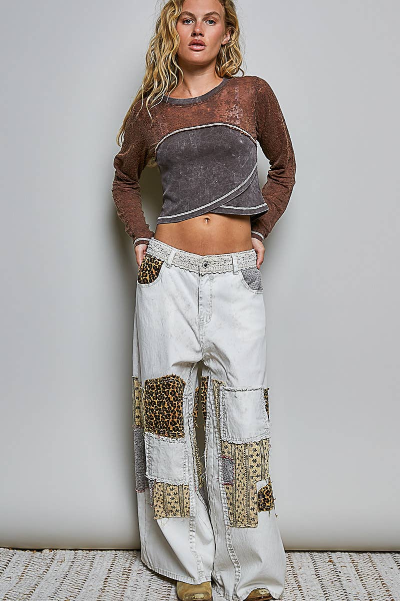 Woman wearing a brown and gray top with white patchwork pants against a plain background