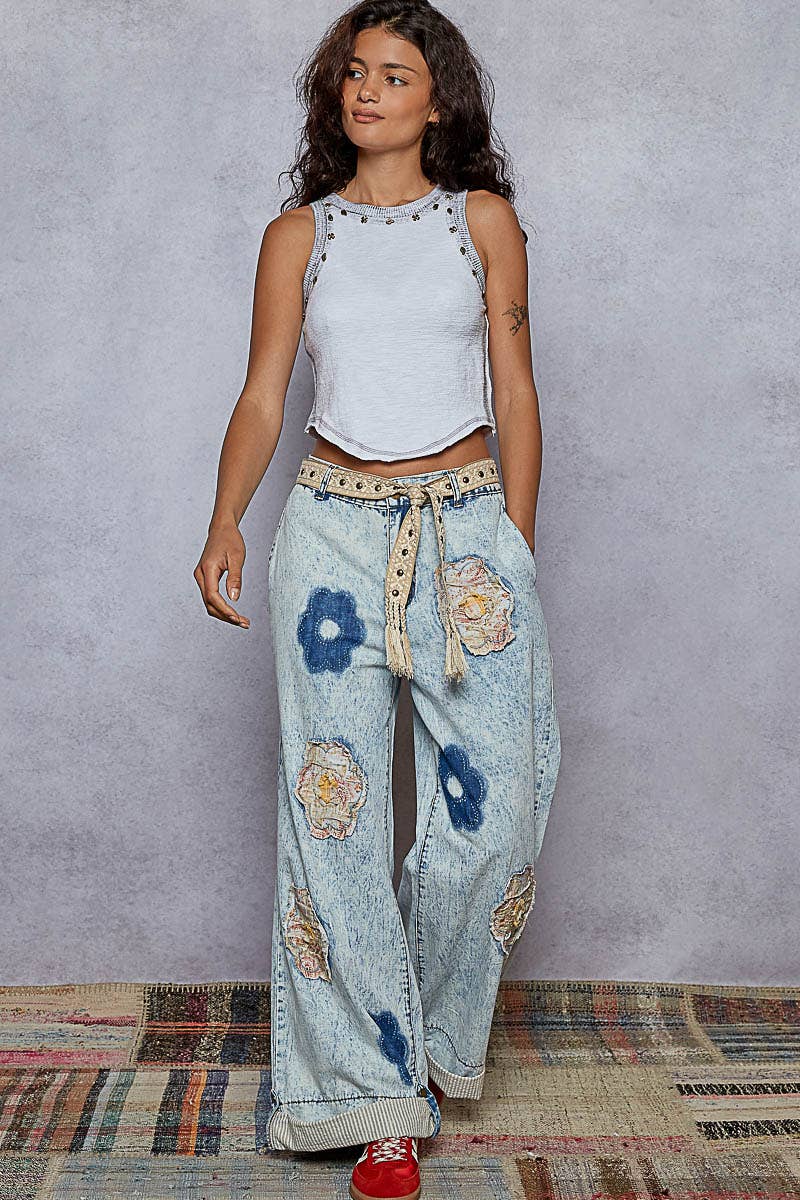 Close-up of a woven black and beige boho belt with stud accents and tassel ends, styled around striped denim jeans with lace patches.