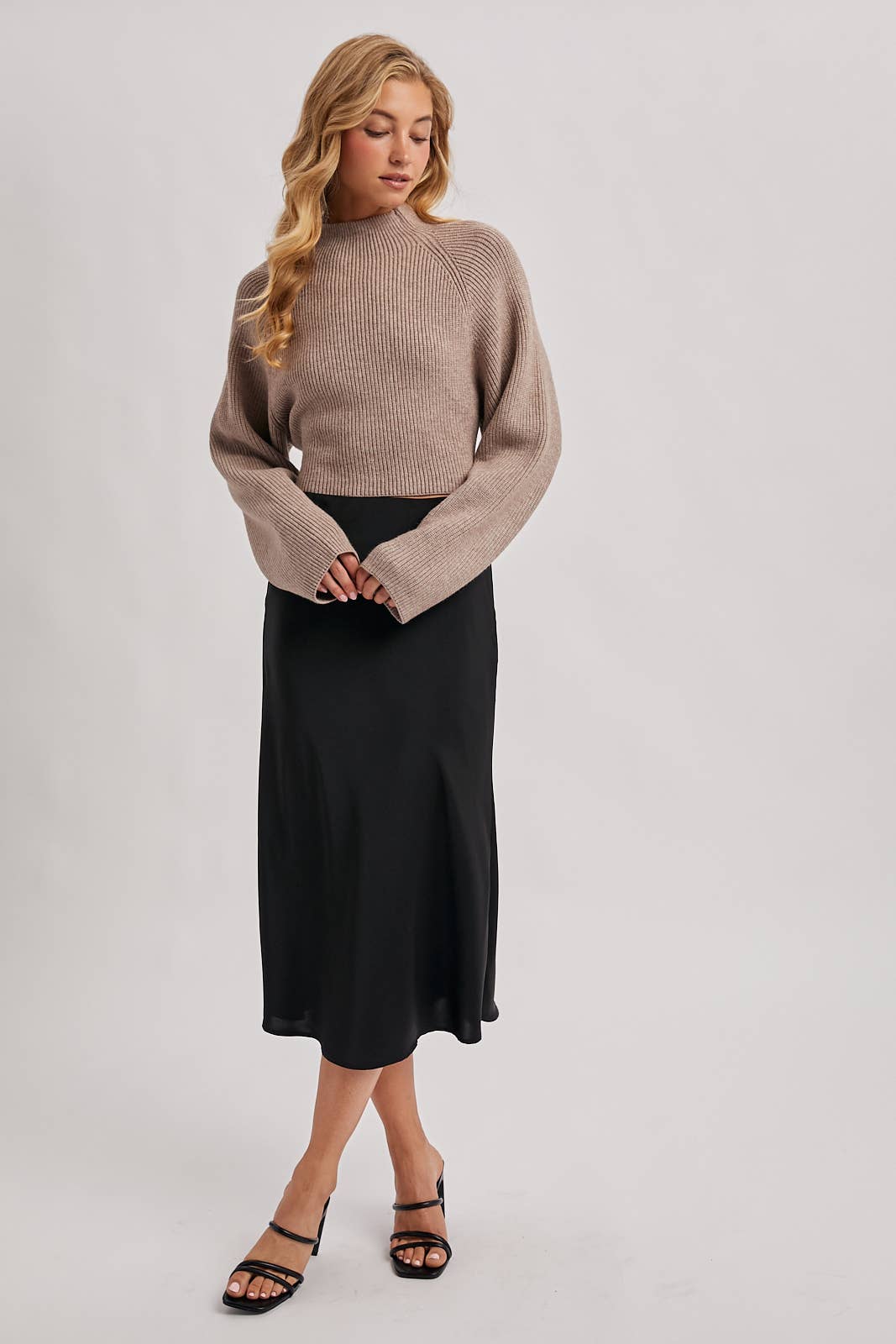 Taupe ribbed mock-neck sweater with wide long sleeves and a cropped fit, styled with a black skirt.