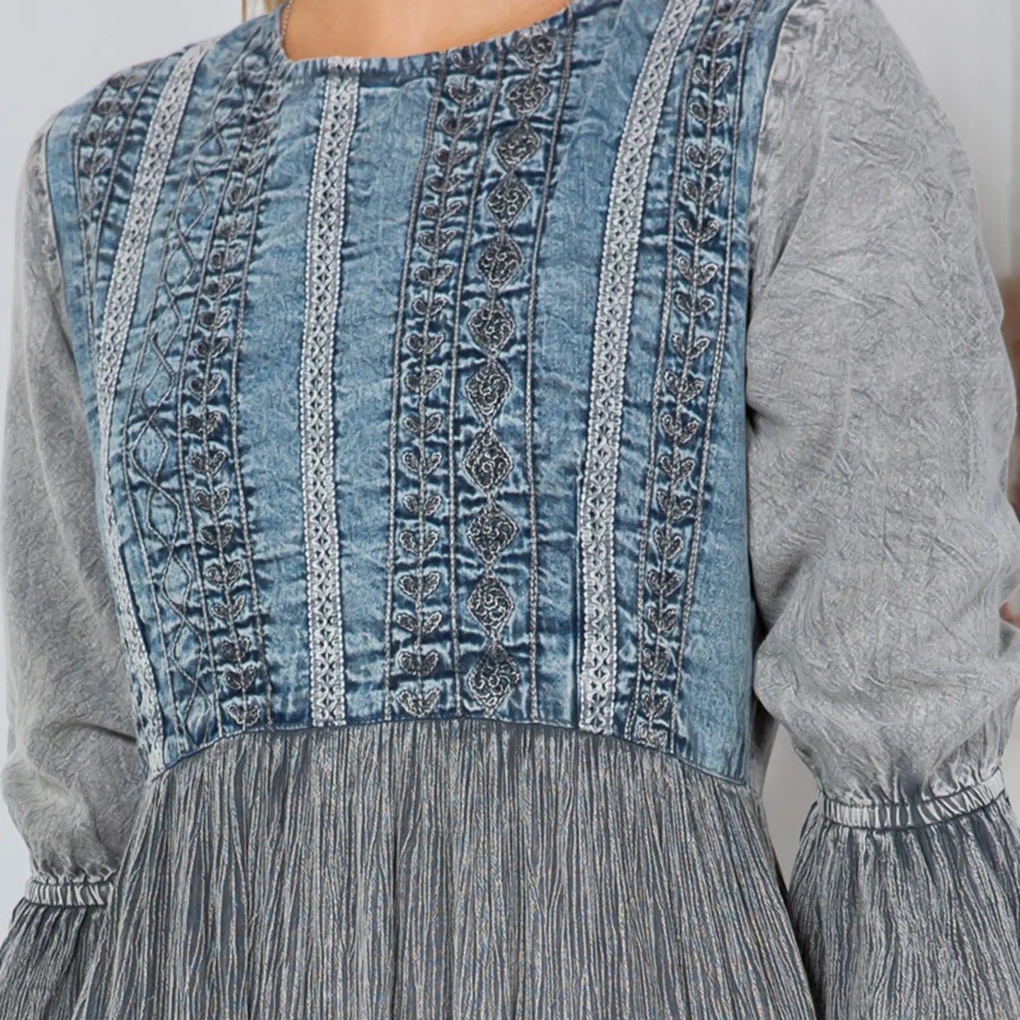Close-up of stonewashed denim bodice with intricate Aari embroidery and lace trim on grey tiered midi dress 