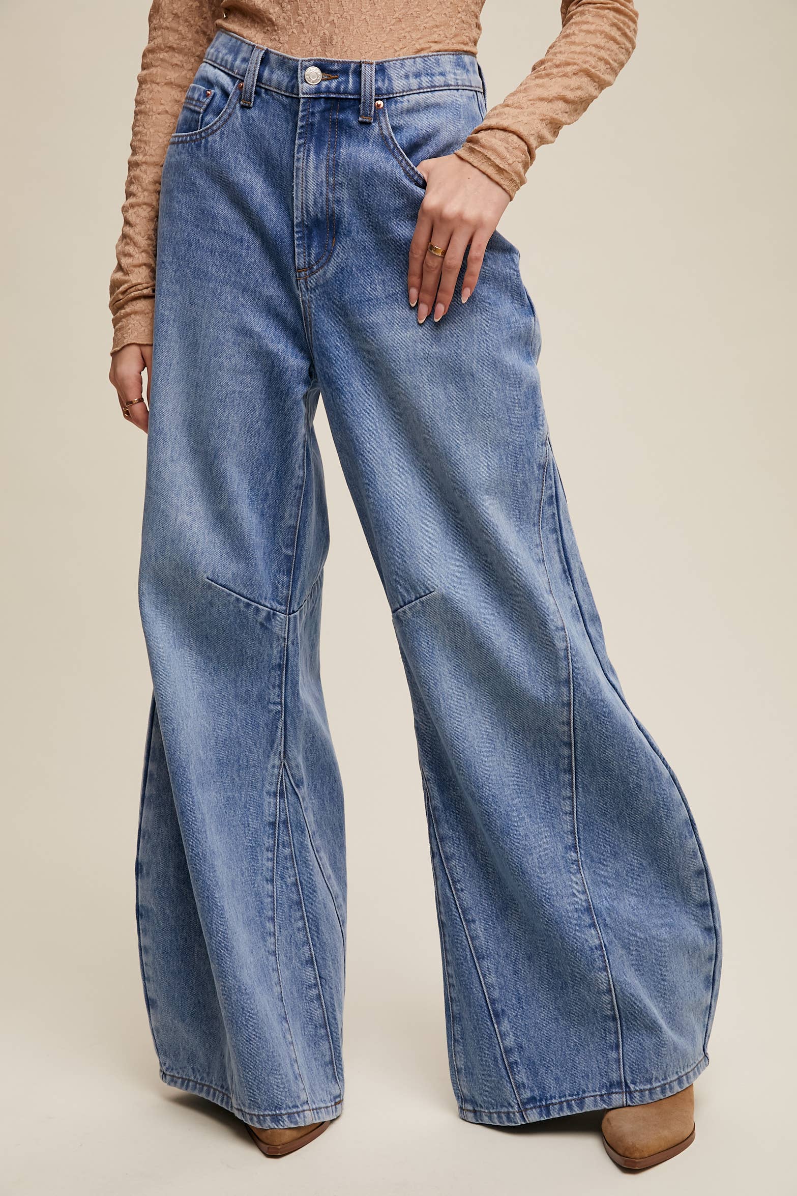 High-rise light-wash wide-leg jeans with front seam panels and knee darts, five-pocket style with zip fly, styled with tan long-sleeve top and pointed-toe boots.