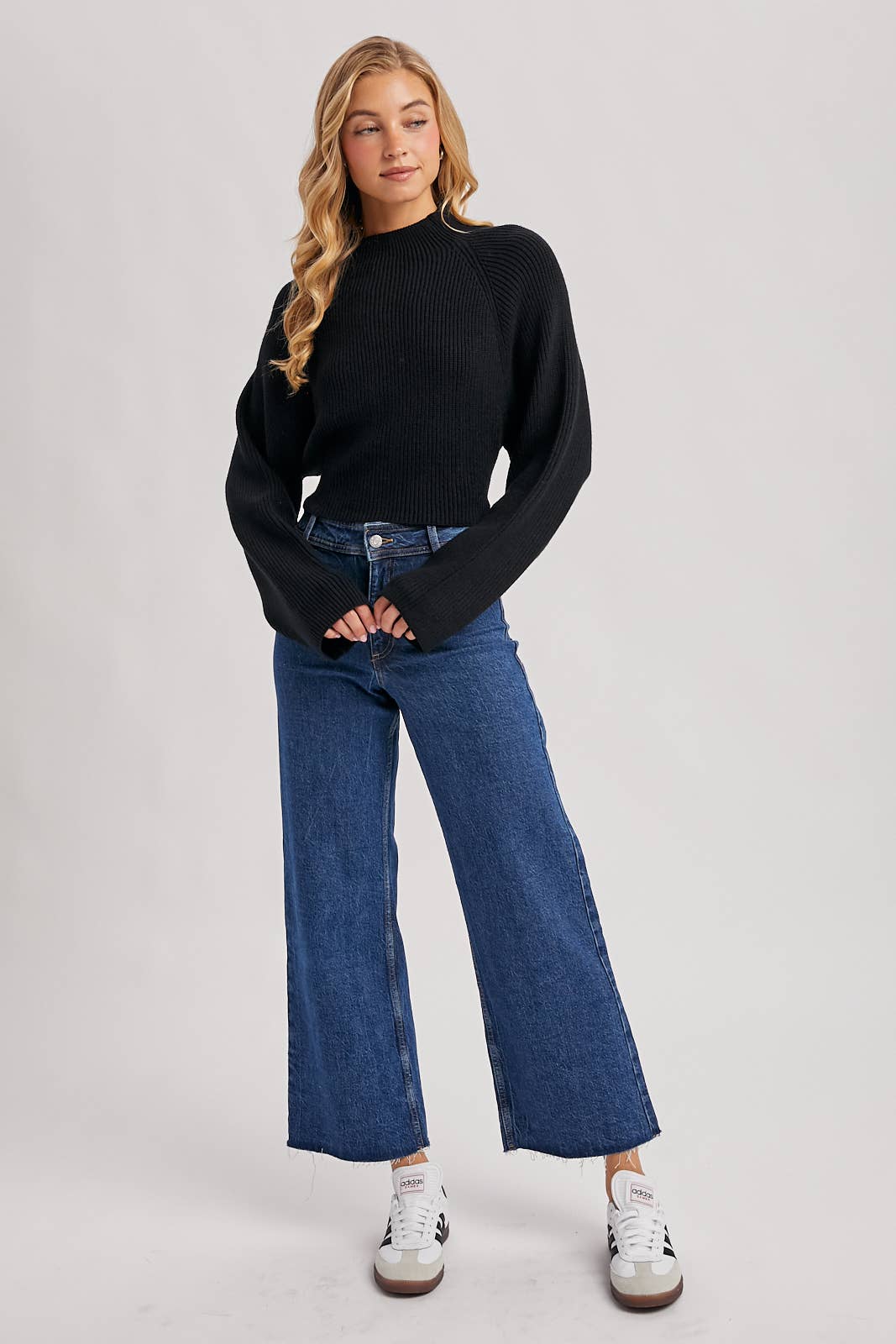 Black ribbed mock-neck sweater with long wide sleeves and a cropped fit, styled with high-rise blue jeans.