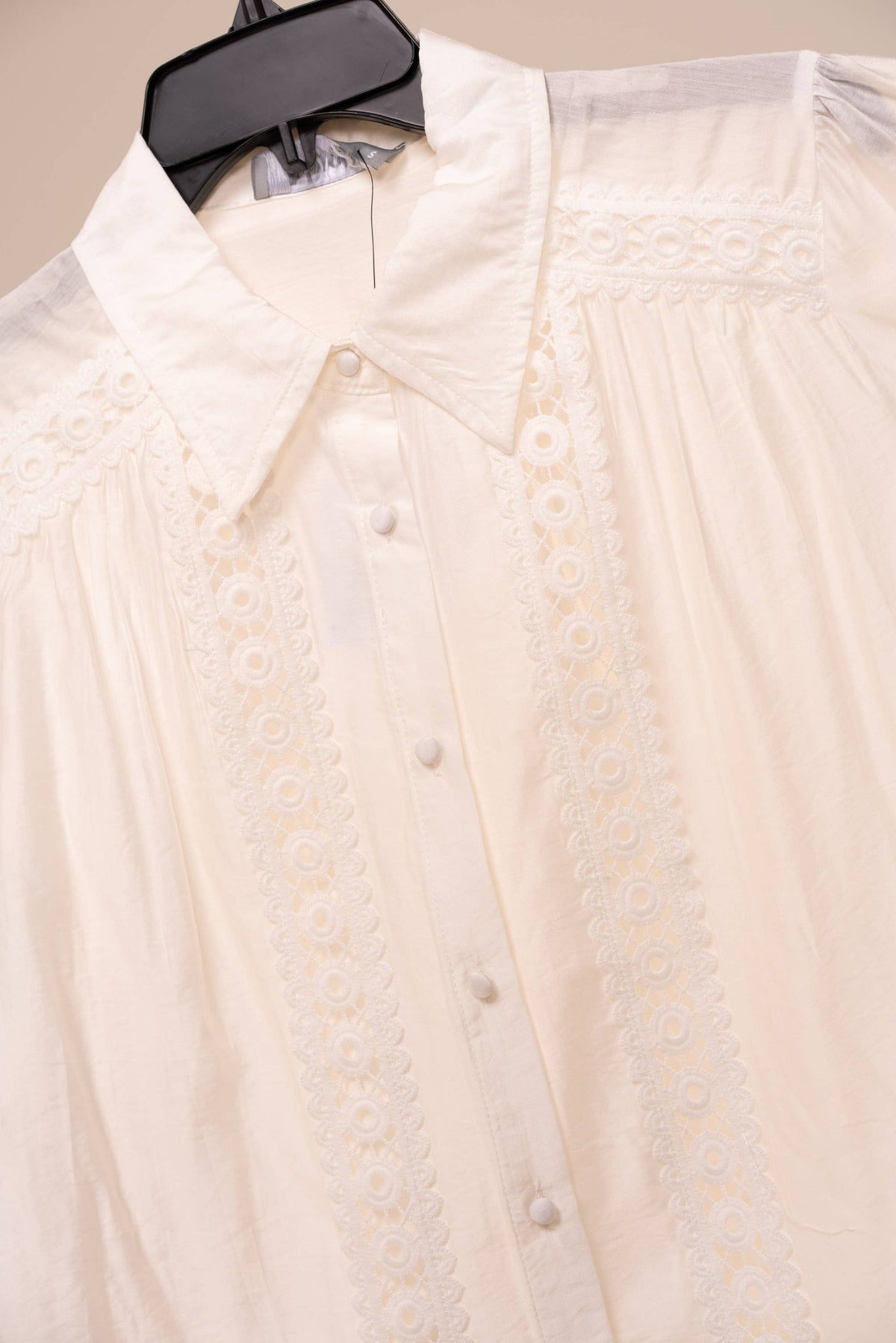 White blouse with lace details on a hanger against a neutral background