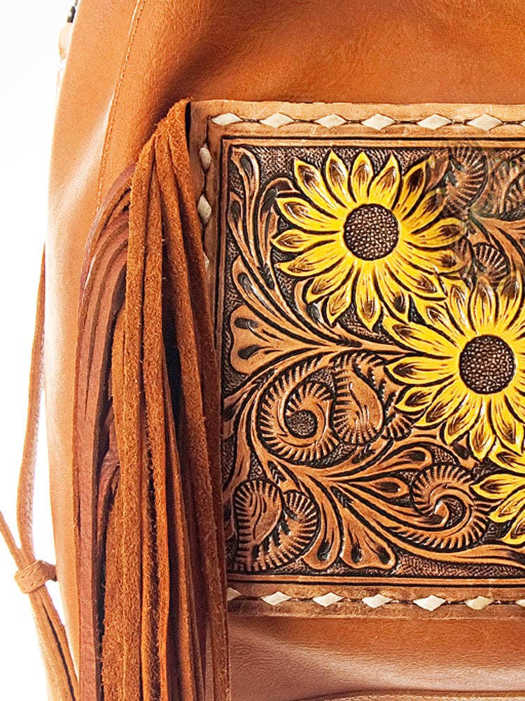Close-up of a brown leather bag featuring a tooled floral panel with two yellow sunflowers and long fringe tassels.
