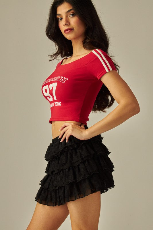 Side view of black lace tiered ruffle mini skirt with elastic waistband, styled with a red graphic crop top.