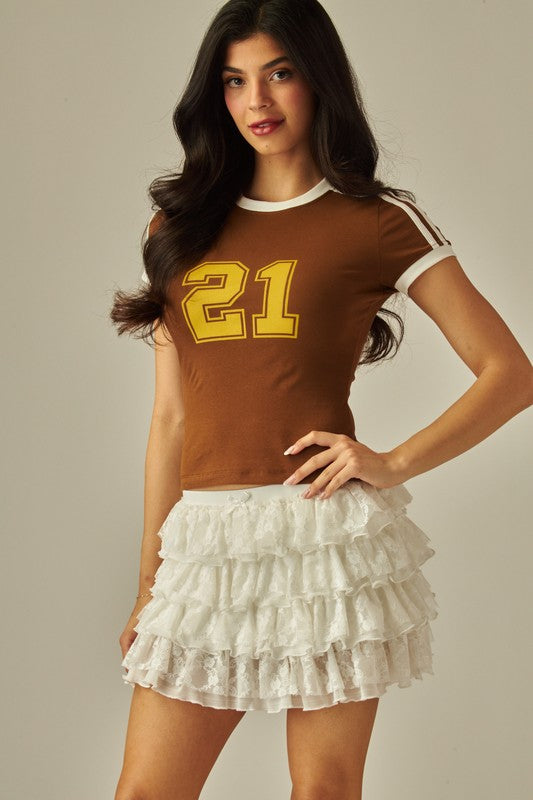 Front view of women’s white lace tiered ruffle mini skirt with elastic waistband, styled with black ankle-strap heels.