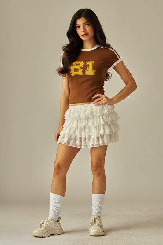 Front view of women’s white lace tiered ruffle mini skirt with elastic waistband, styled with black ankle-strap heels.