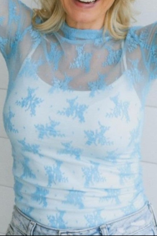 Sheer blue lace mesh long-sleeve top layered over a white bralette, styled with distressed low-rise jeans.