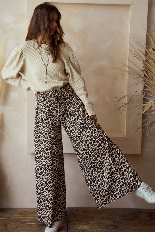 Front view — leopard print wide-leg pants with high rise and tie waist, flowy woven drape; styled with a beige knit sweater on model.